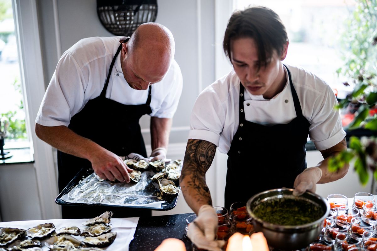 Two chefs in a restaurant kitchen preparing gourmet dishes with fresh ingredients and focused expressions